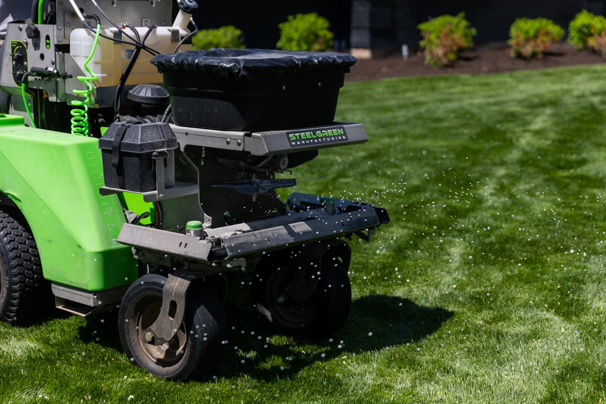 lawn care technician spreading granular fertilzer on a nice lawn